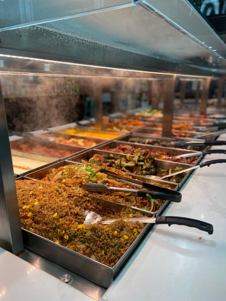 Two rows of 10 buffet style trays with steaming dresh food from ETC Eatery near Herald Square New York City