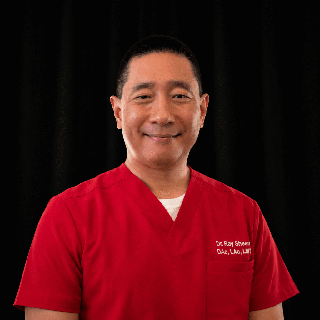 Massage therapist ray in a red scrub top with a black background.